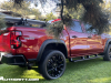 2023-chevrolet-colorado-trail-boss-radiant-red-tintcoat-gnt-first-drive-exterior-006-side-rear-three-quarters-accessory-wheels-steps-exhaust-tip-tonneau-cover-removable-rail-kit-by-thule-surf-board