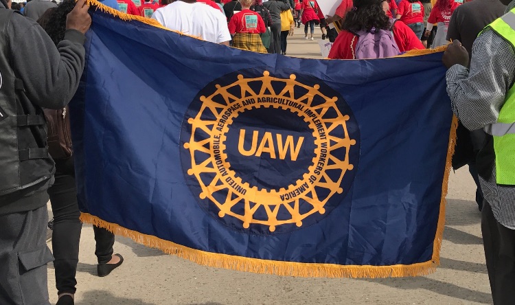 Workers carry a UAW flag while on strike.