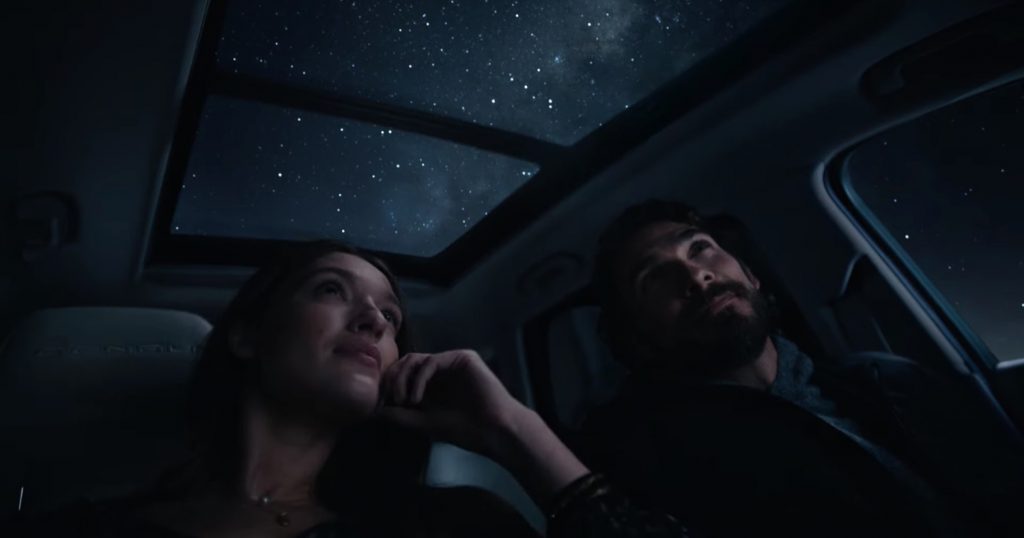 A pair of passengers look at the night sky through the sunroof of the 2023 GMC Terrain.