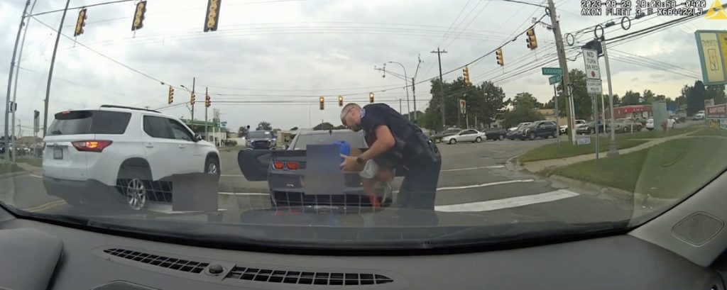 Photo of Officer Fraser tapping the baby's back behind the Chevy Camaro.