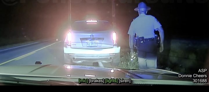 A police officer approaches a Cadillac SRX during a traffic stop.