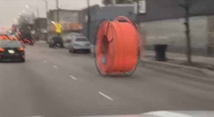 A massive cable spool rolls down a busy street before colliding with a Chevy Malibu.