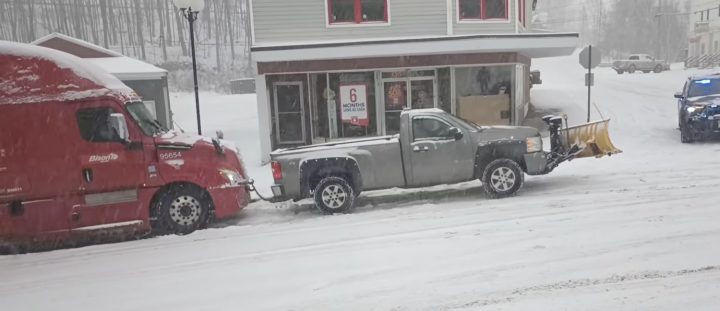 A Chevy Silverado pulls a semi up a snowy hill.