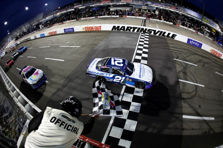 Photo of the No. 21 NASCAR Chevy of Austin Hill crossing the start/finish line to win the Xfinity race at Martinsville. The field can be seen wrecking behind him.