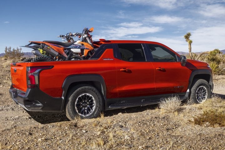 Side rear three-quarters view of 2026 Chevy Silverado EV Trail Boss with motorcycles in the bed. Chevy Silverado EV deals include interest-free financing in June 2025.