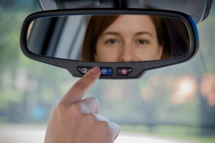 View of a woman reflected in the rearview mirror pressing the OnStar button.