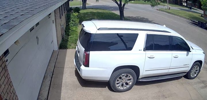 A white GMC Yukon XL reverses up a driveway.