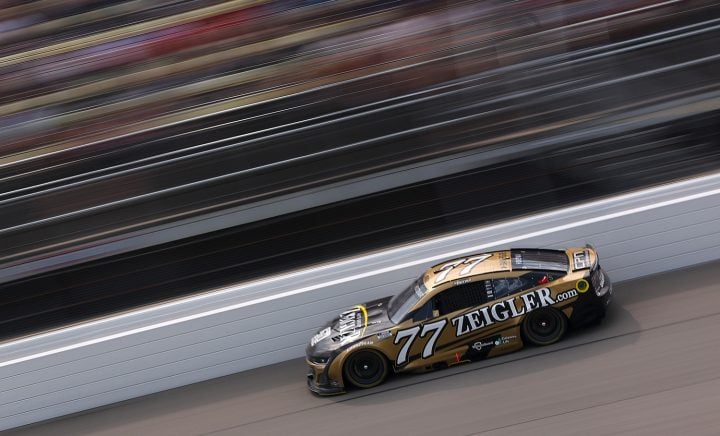 Photo of the No. 77 NASCAR Chevy of Carson Hocevar on track at Michigan, pictured from a side angle. Hocevar was fined by his own team for making culturally insensitive comments about Mexico. 